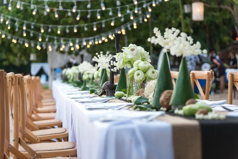 A decorated table with a white table cloth, decorations and tan chairs.